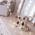 Pair of earrings with red and green beads on a decorative stand with fairy lights.